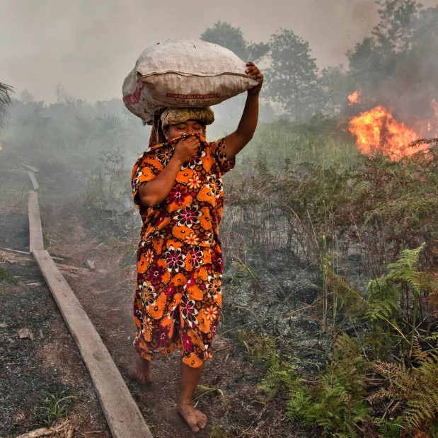 Woman covering mouth with fabric and fire burning behind her